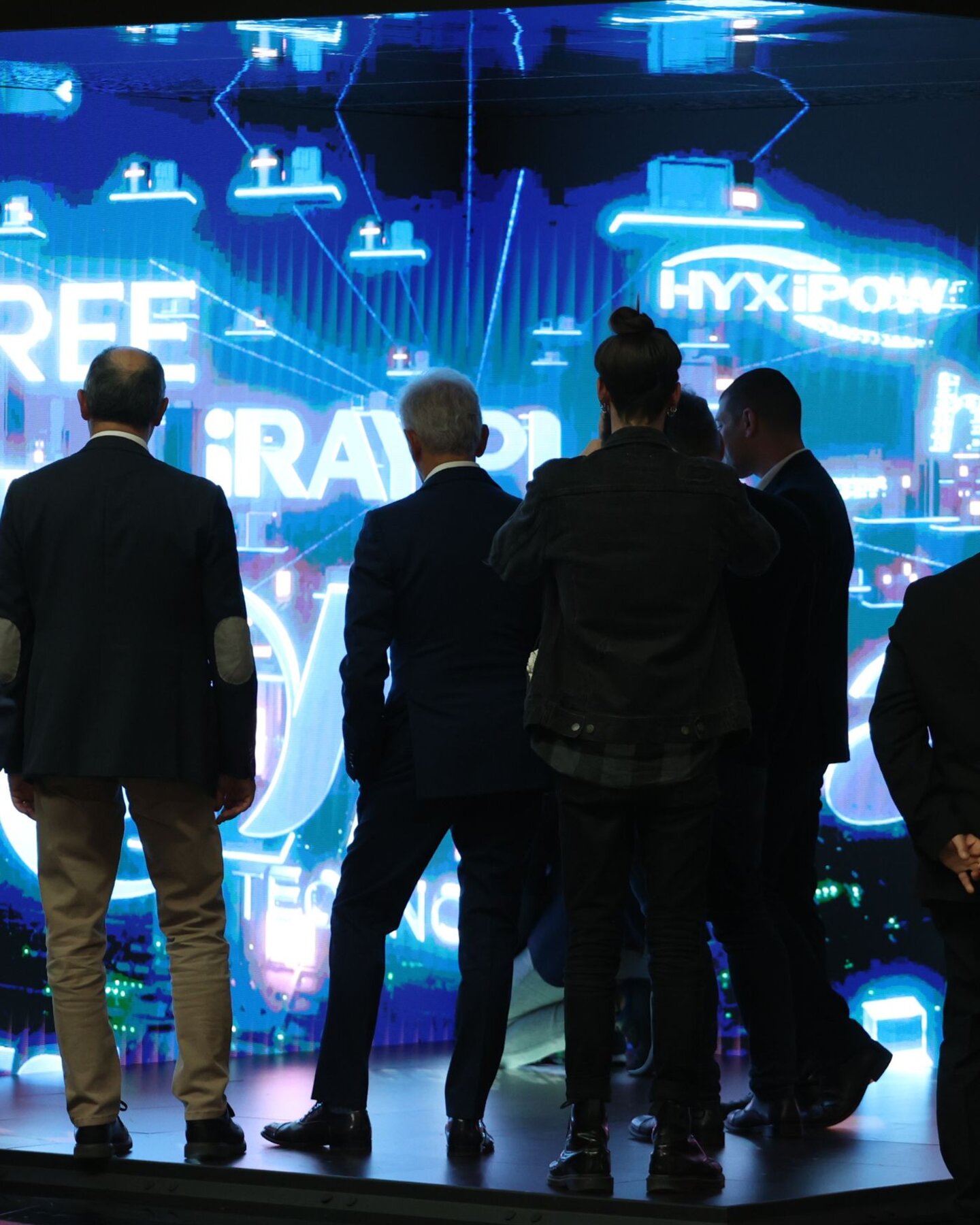 Visitatori osservano un grande schermo LED con loghi e proiezioni digitali durante la fiera MIR a Rimini