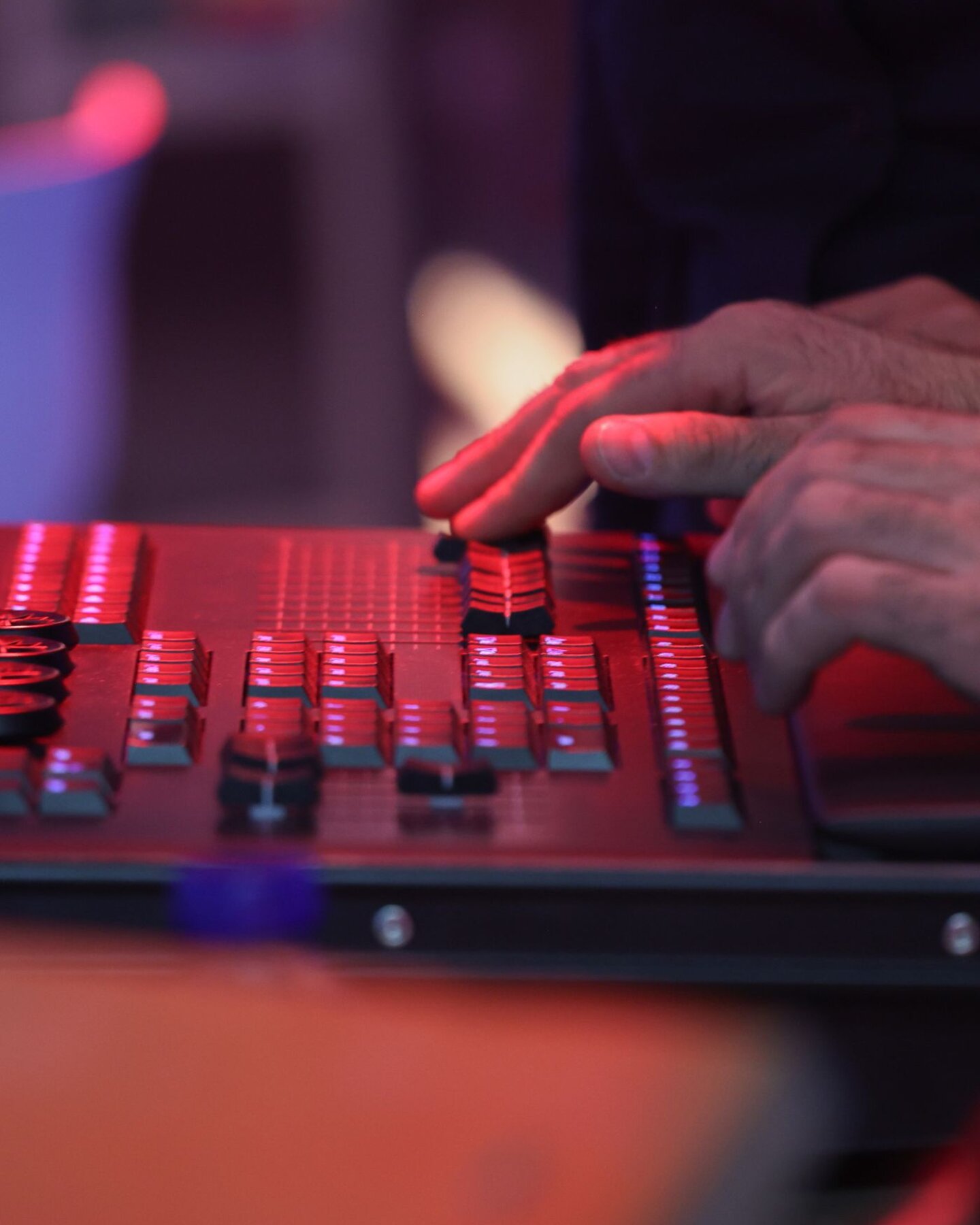 Mani che regolano i controlli di una console luci professionale durante la gestione tecnica di uno spettacolo live